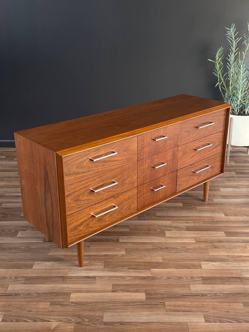 Wooden dresser with multiple drawers on a wooden floor against a dark wall.
