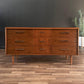 Wooden dresser with six drawers on a wooden floor against a dark wall.