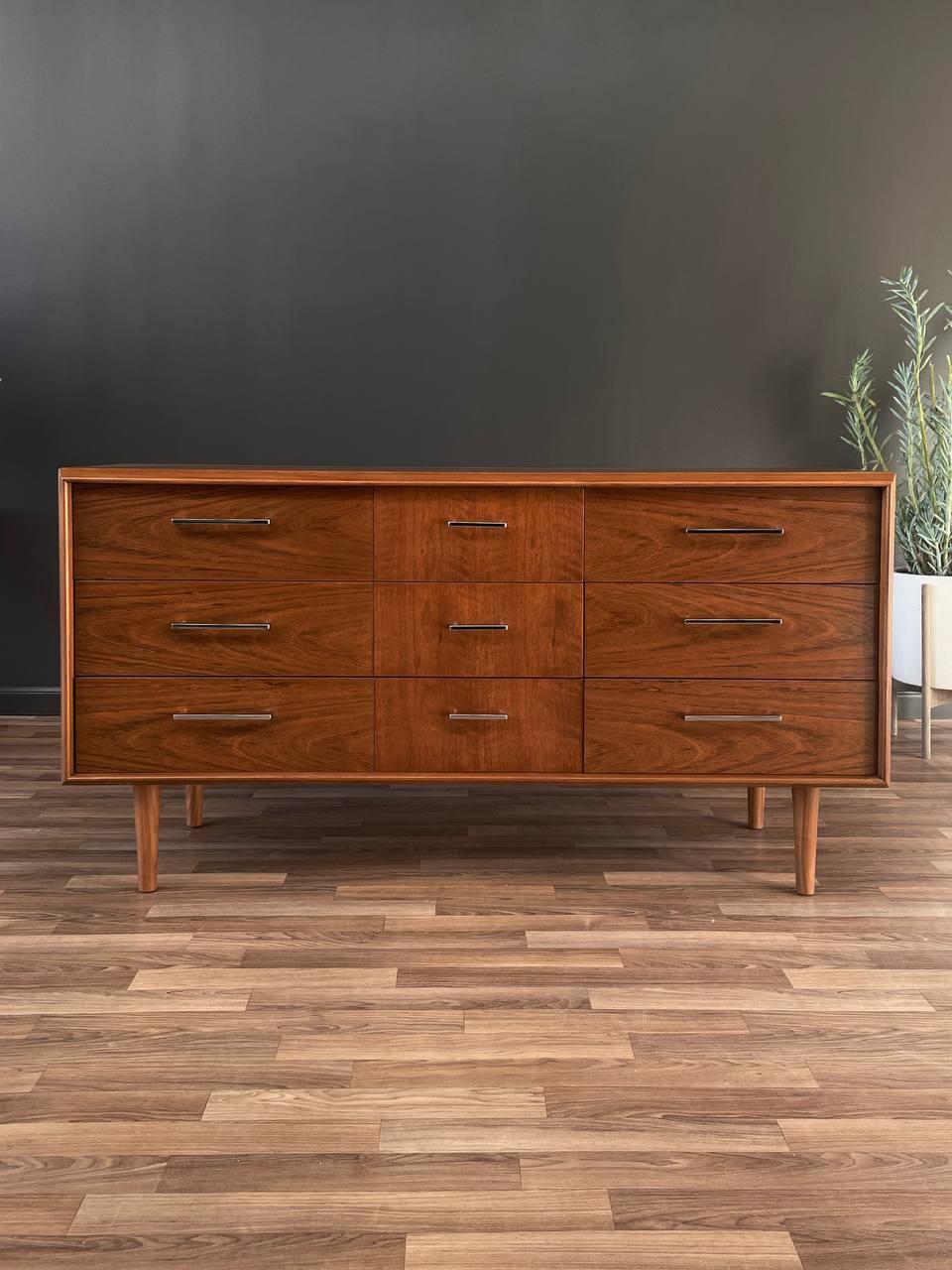 Wooden dresser with six drawers on a wooden floor against a dark wall.