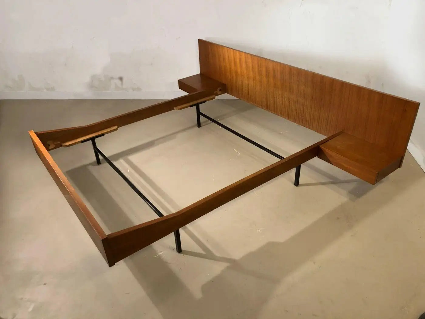 Wooden bed frame with headboard on a concrete floor.