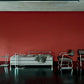 Modern bedroom with a bed, chairs, and lamps against a red wall.