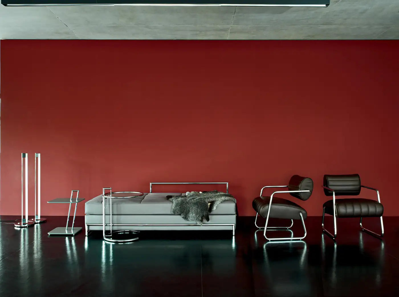 Modern bedroom with a bed, chairs, and lamps against a red wall.