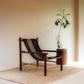 Wooden chair with woven backrest in a minimalistic room with a plant and rug.